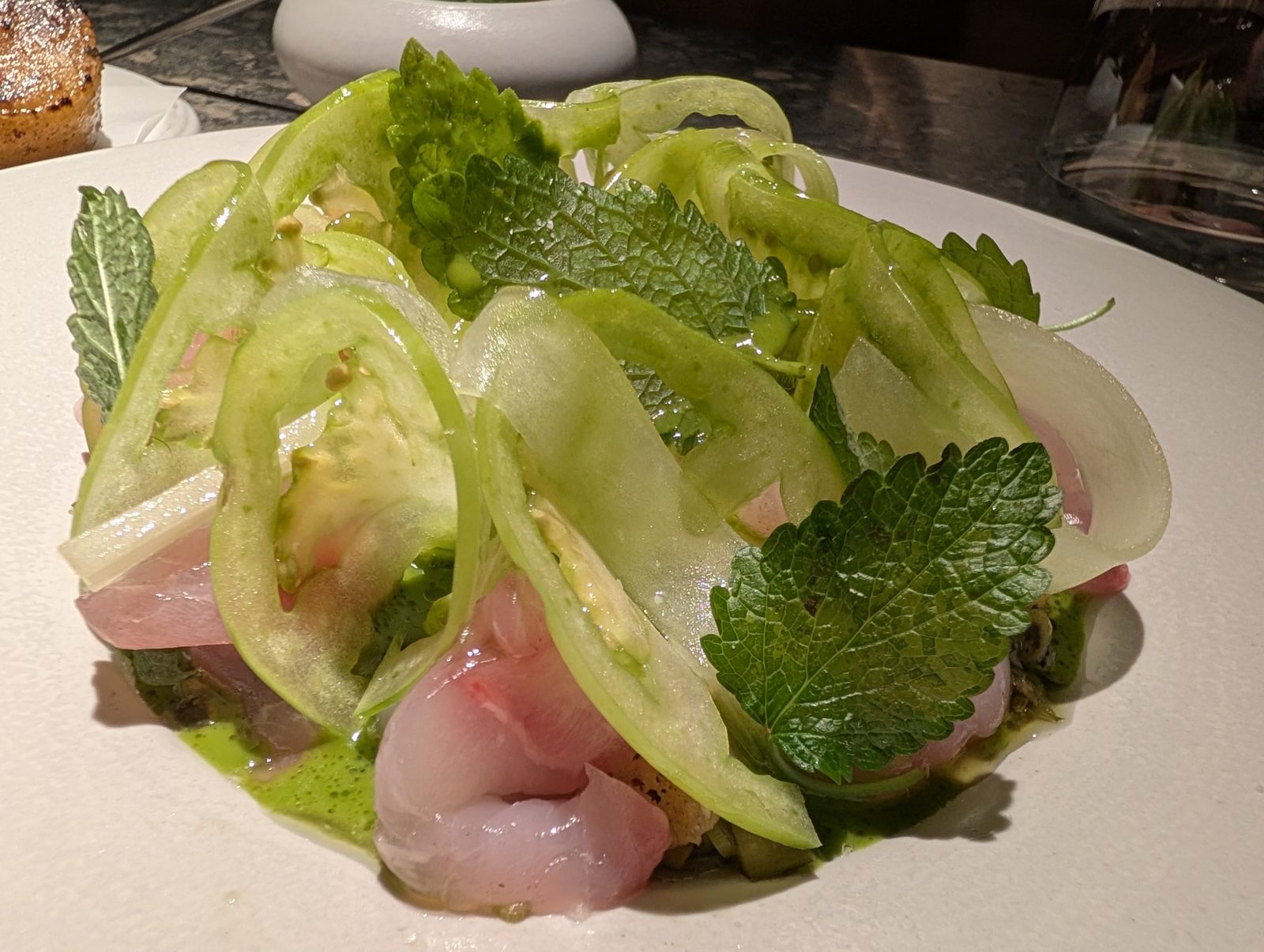 Raw fish under green tomato and mint.